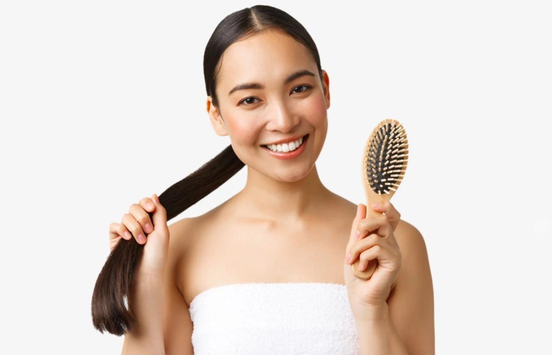 A woman standing with bunch of hairs in one hand and a comb in other.